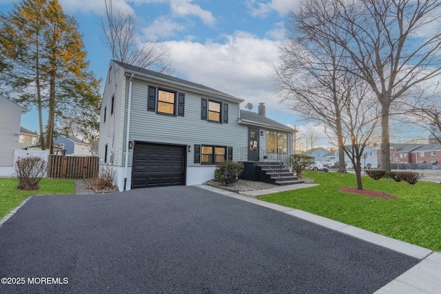 split level home featuring driveway, a front lawn, fence, an attached garage, and a chimney