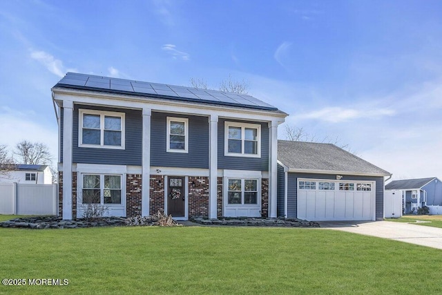 greek revival inspired property featuring a front lawn, roof mounted solar panels, fence, concrete driveway, and an attached garage