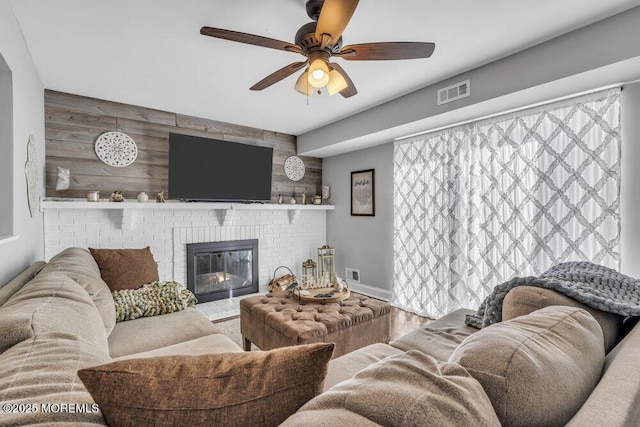 living room with wooden walls, visible vents, a brick fireplace, an accent wall, and a ceiling fan