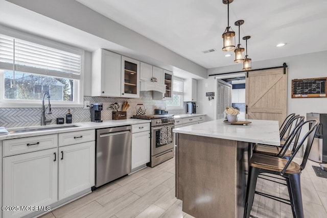 kitchen featuring visible vents, a sink, appliances with stainless steel finishes, a barn door, and tasteful backsplash