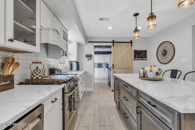 kitchen with visible vents, tasteful backsplash, stainless steel appliances, a barn door, and white cabinets