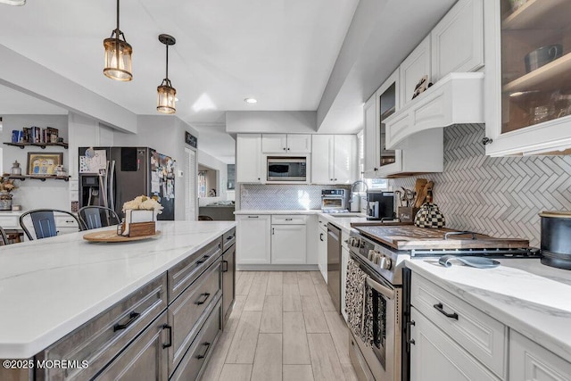 kitchen with a sink, decorative backsplash, hanging light fixtures, white cabinets, and appliances with stainless steel finishes