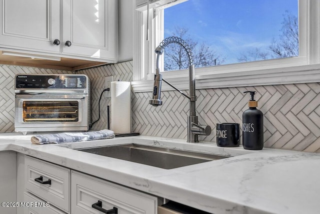 interior space with light stone counters, a toaster, backsplash, and white cabinetry