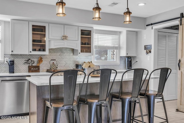 kitchen featuring stainless steel dishwasher, a barn door, a breakfast bar area, and visible vents