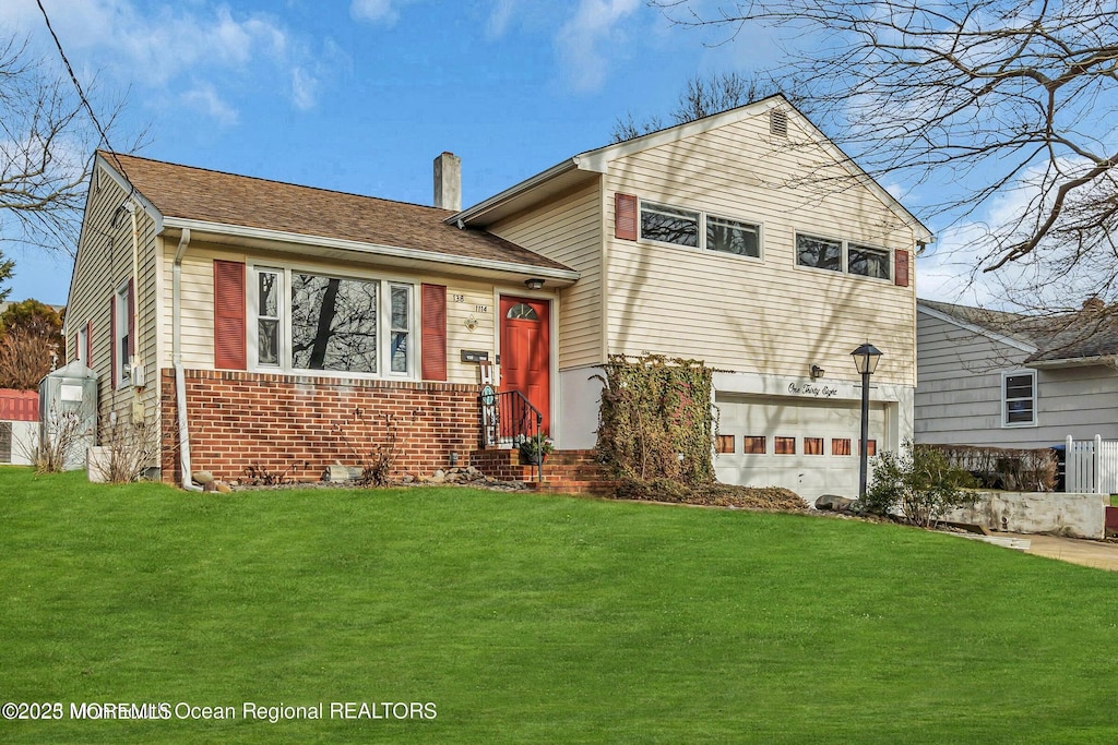 tri-level home with a chimney, a garage, a front lawn, and brick siding