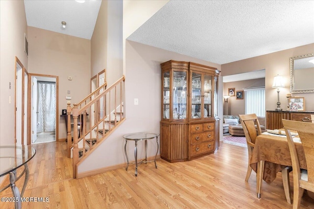 dining space featuring stairway, baseboards, light wood-style floors, and a textured ceiling