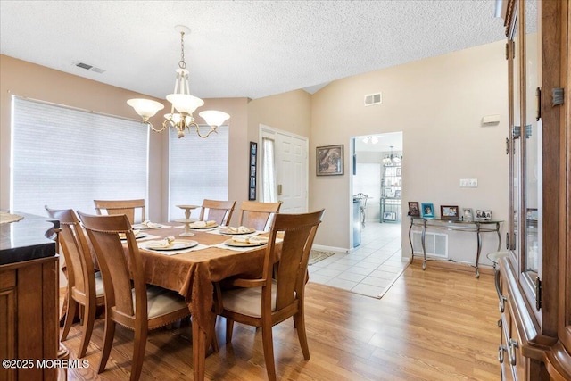 dining room with visible vents, light wood-style flooring, a textured ceiling, lofted ceiling, and a chandelier