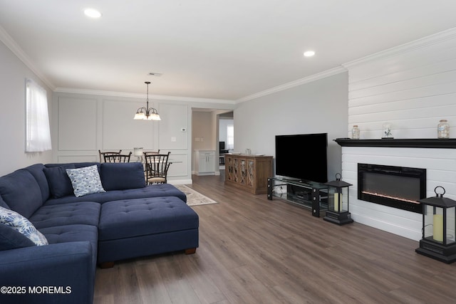 living area featuring a chandelier, a glass covered fireplace, ornamental molding, wood finished floors, and a decorative wall