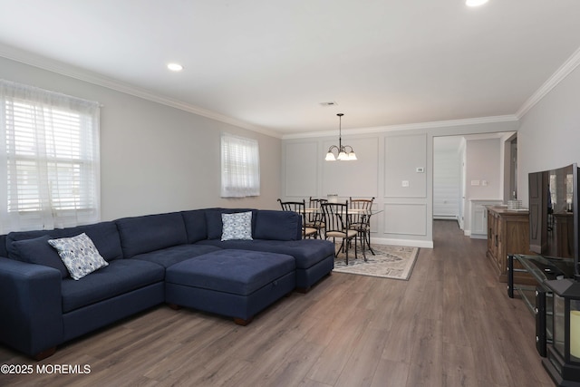 living room with wood finished floors, visible vents, crown molding, a decorative wall, and a notable chandelier