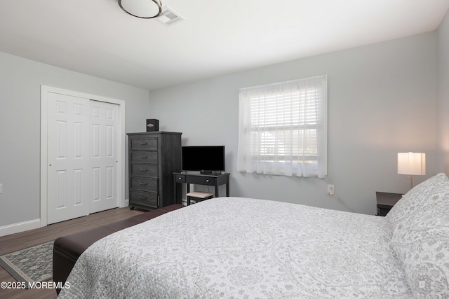 bedroom with a closet, visible vents, baseboards, and wood finished floors