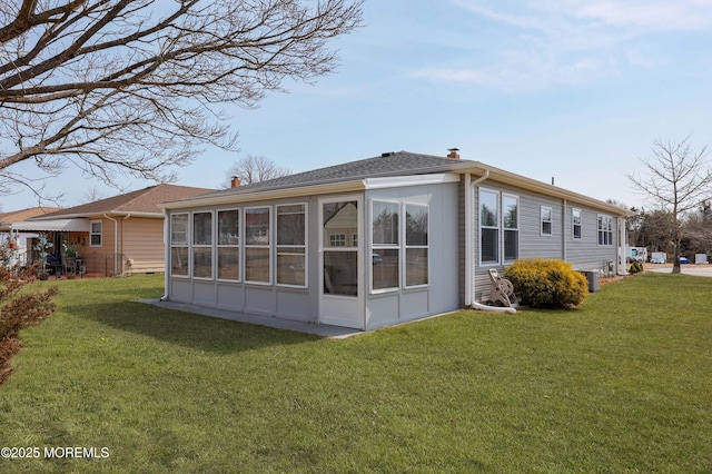 back of property with a yard, central AC unit, a sunroom, and a shingled roof