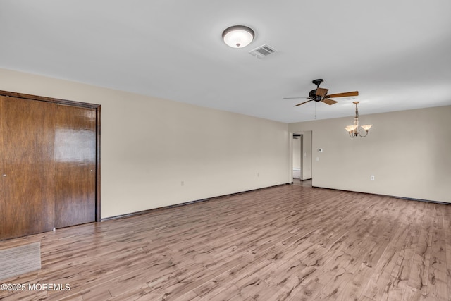 empty room featuring ceiling fan with notable chandelier, visible vents, and light wood-type flooring