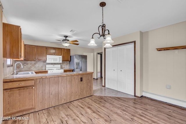 kitchen with light wood finished floors, white appliances, a peninsula, and a sink