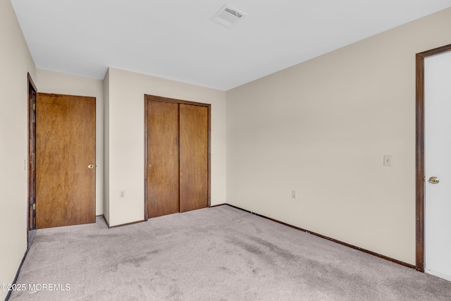 unfurnished bedroom with a closet, visible vents, light colored carpet, and baseboards