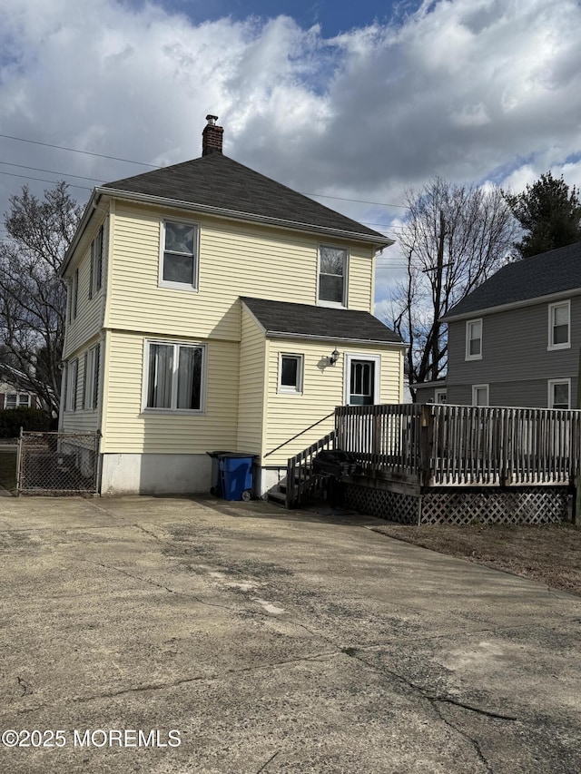 rear view of property featuring a chimney, a deck, and fence