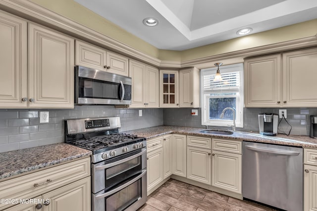 kitchen featuring light wood finished floors, a sink, appliances with stainless steel finishes, cream cabinets, and backsplash