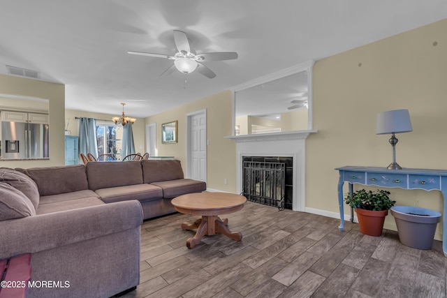 living room featuring baseboards, wood finished floors, a fireplace, and ceiling fan with notable chandelier