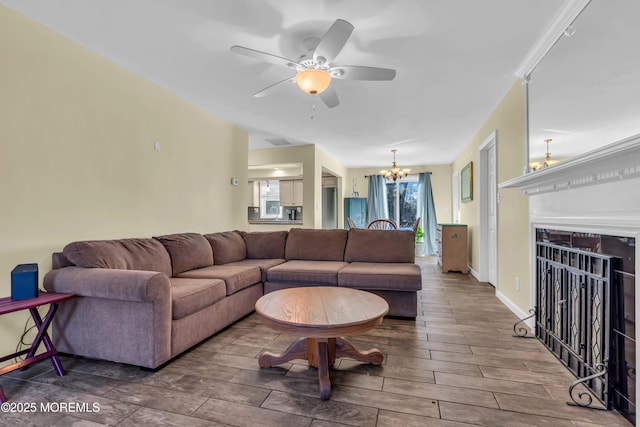 living room with a fireplace, ceiling fan with notable chandelier, baseboards, and wood finish floors