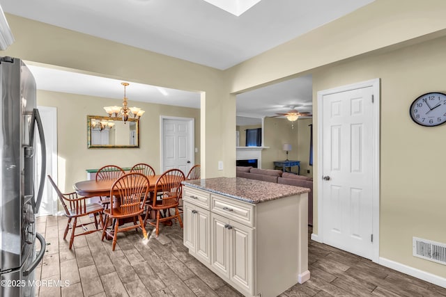 kitchen featuring visible vents, light stone countertops, wood tiled floor, stainless steel fridge with ice dispenser, and a fireplace