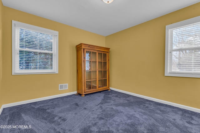 unfurnished room with visible vents, dark colored carpet, and baseboards