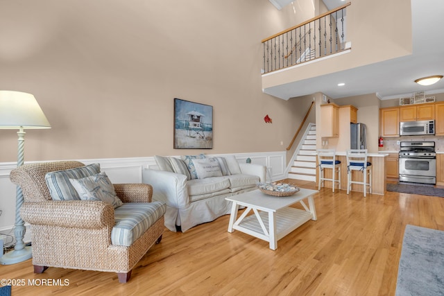 living room featuring a wainscoted wall, stairway, light wood-style floors, a decorative wall, and a towering ceiling