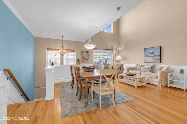 dining space with a chandelier, crown molding, light wood-type flooring, and a high ceiling