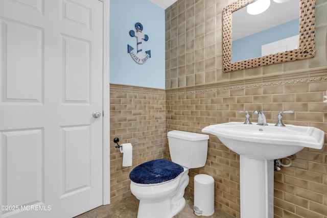 bathroom with wainscoting, toilet, and tile walls