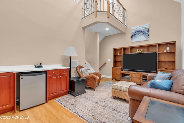 living area with visible vents, stairs, light wood-type flooring, and a high ceiling