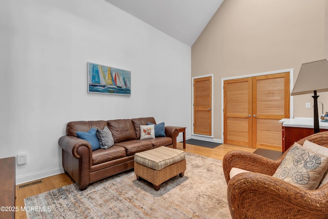 living room with high vaulted ceiling, wood finished floors, visible vents, and baseboards