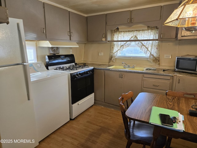 kitchen with washer / dryer, freestanding refrigerator, a sink, gas range oven, and under cabinet range hood