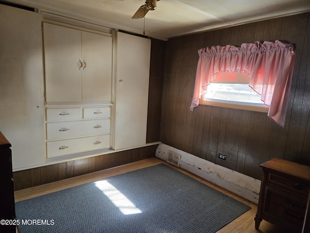 unfurnished bedroom featuring wooden walls, a ceiling fan, and wood finished floors