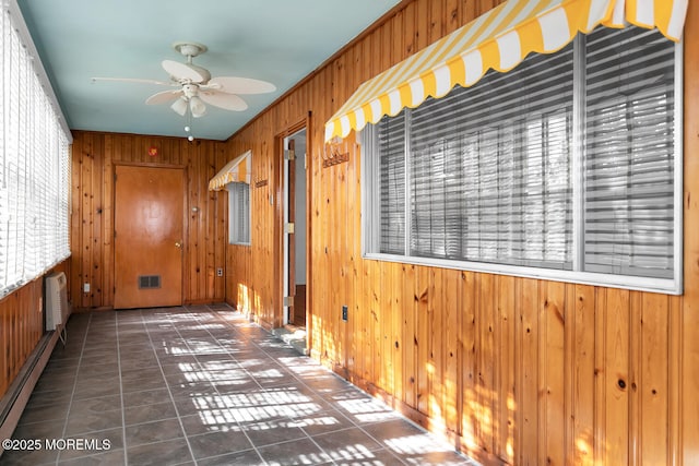 hall featuring a baseboard radiator, wooden walls, visible vents, and tile patterned flooring