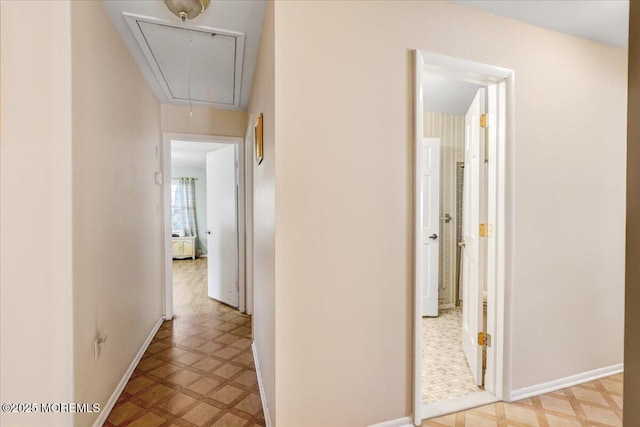 hallway with baseboards, light floors, and attic access