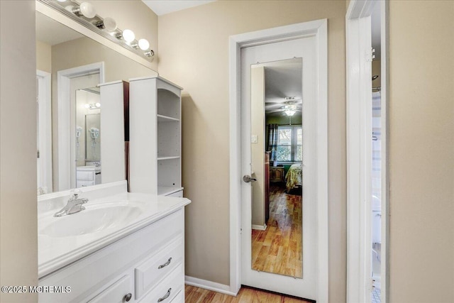 bathroom featuring baseboards, a ceiling fan, wood finished floors, and vanity