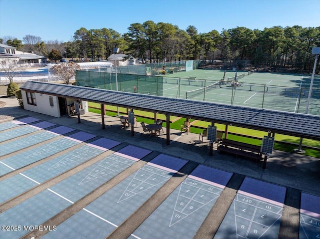 view of property's community with a tennis court, covered parking, shuffleboard, and fence