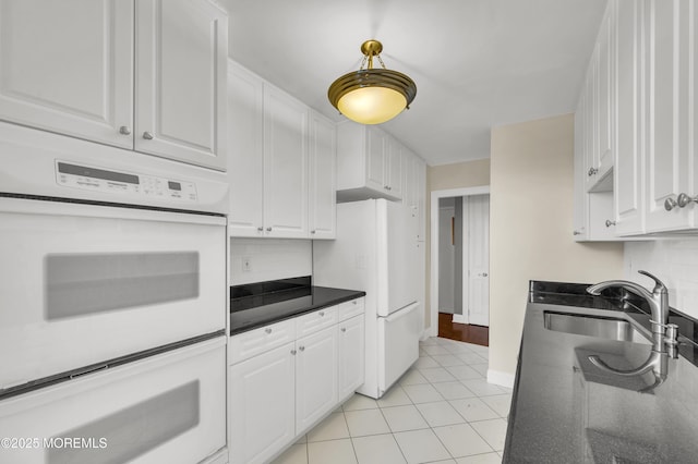 kitchen featuring dark countertops, white appliances, white cabinetry, and a sink