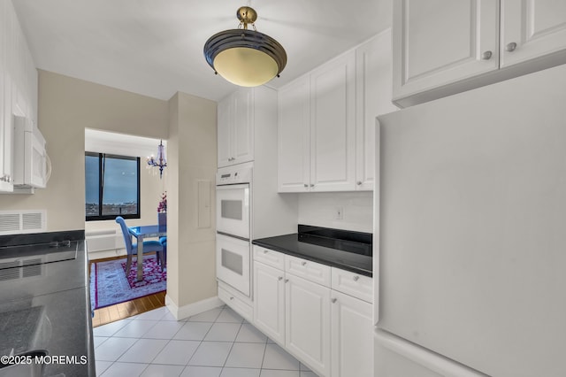 kitchen featuring light tile patterned floors, a notable chandelier, white appliances, and white cabinetry