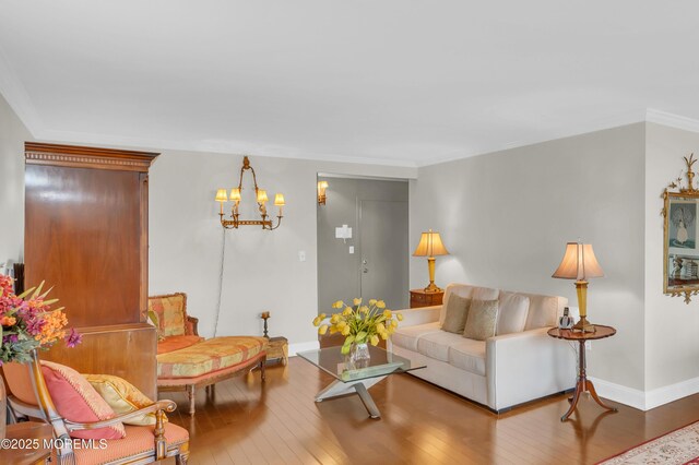 living room with baseboards, wood-type flooring, a chandelier, and crown molding