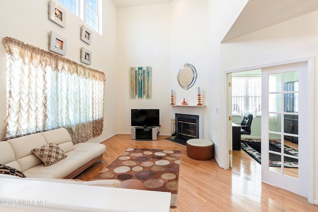 living area featuring plenty of natural light, wood finished floors, a fireplace with flush hearth, and a towering ceiling