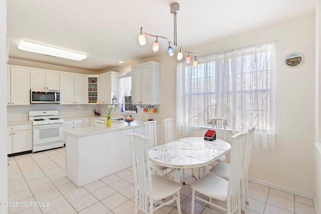 kitchen featuring white range with gas cooktop, stainless steel microwave, tasteful backsplash, a peninsula, and light tile patterned flooring