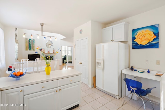 kitchen featuring pendant lighting, white refrigerator with ice dispenser, white cabinets, light countertops, and light tile patterned floors