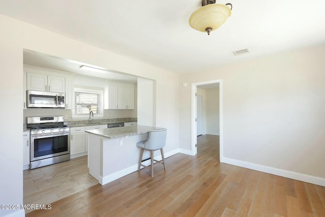 kitchen with white cabinets, appliances with stainless steel finishes, light wood-style floors, and a sink