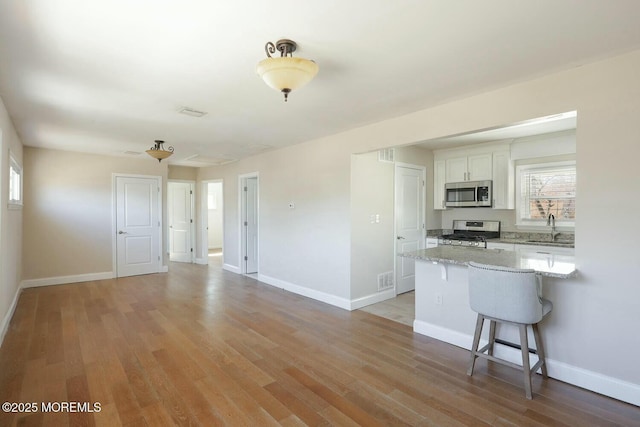 kitchen with light wood-style flooring, a sink, white cabinetry, stainless steel appliances, and a breakfast bar area