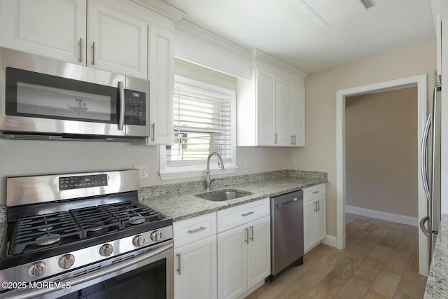 kitchen featuring light stone counters, baseboards, a sink, appliances with stainless steel finishes, and white cabinetry