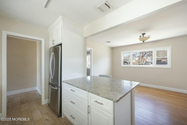 kitchen featuring light stone countertops, visible vents, baseboards, light wood-style flooring, and freestanding refrigerator