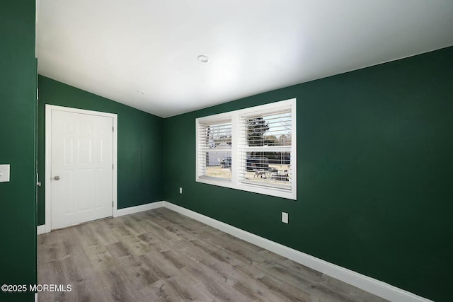 spare room with wood finished floors, baseboards, and vaulted ceiling