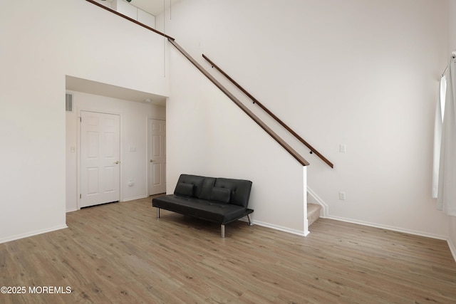 sitting room with visible vents, light wood-style flooring, stairway, a high ceiling, and baseboards