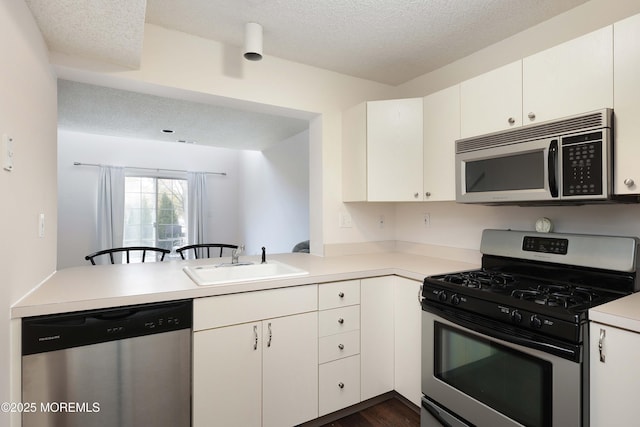 kitchen featuring a sink, a textured ceiling, white cabinetry, stainless steel appliances, and light countertops