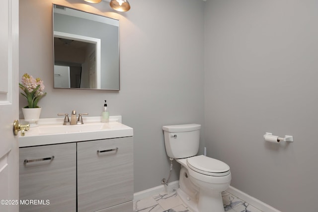 half bathroom with baseboards, toilet, marble finish floor, and vanity