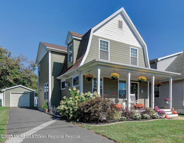 view of front of house with an outbuilding, driveway, a front lawn, a detached garage, and a porch